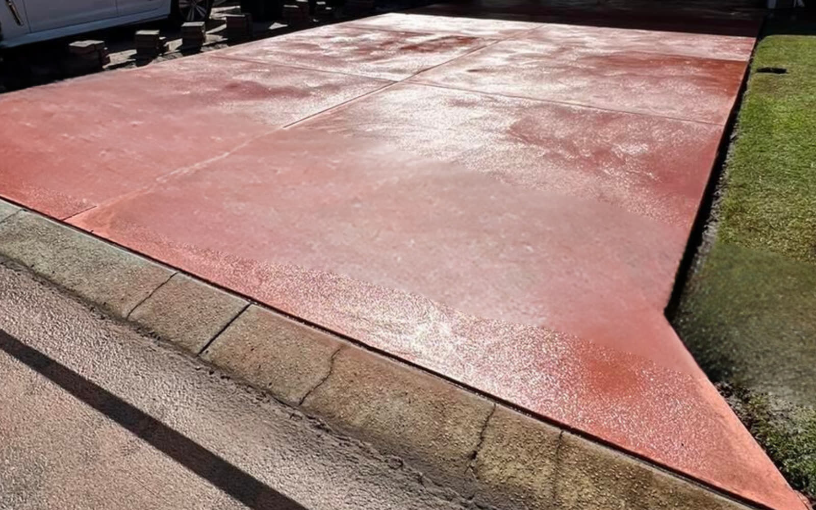 Red oxide coloured concrete driveway meeting the kerb